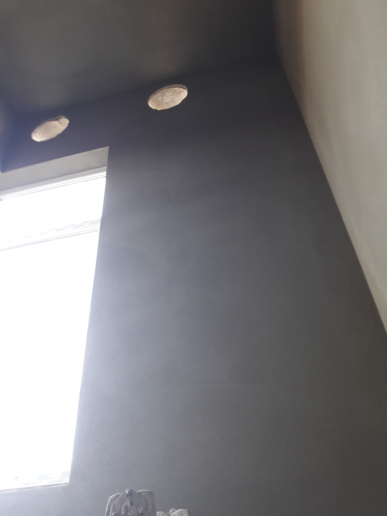 Świeżo położona szara gładź na ścianie w Pałecznicy, z widocznymi otworami na oświetlenie sufitowe i oknem po lewej stronie, uchwycona pod kątem z dołu.