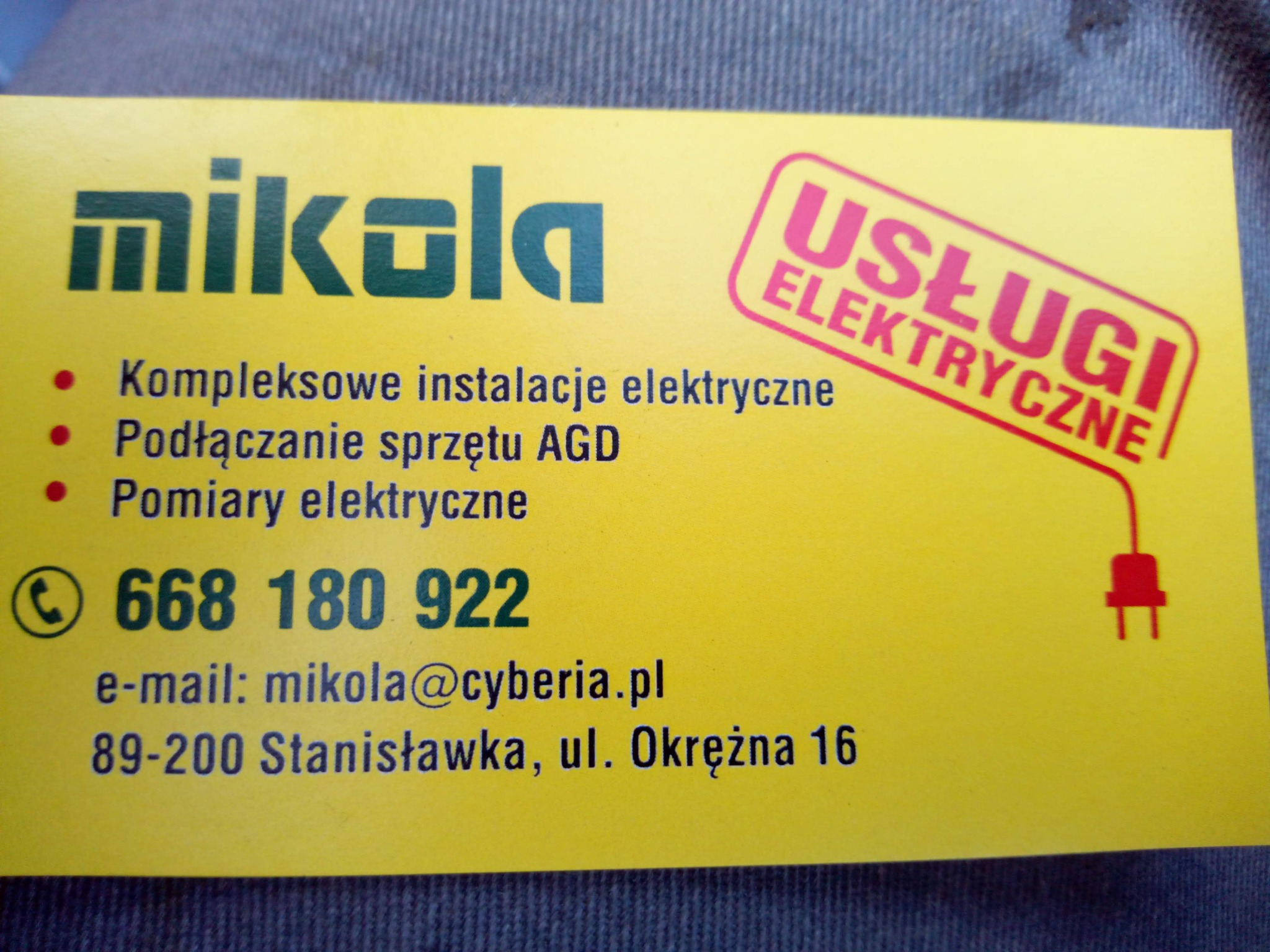 Żółta wizytówka firmy z logo 'mikala', oferującej kompleksowe instalacje elektryczne, podłączanie sprzętu AGD i pomiary elektryczne, z numerem telefonu, adresem e-mail i adresem siedziby.