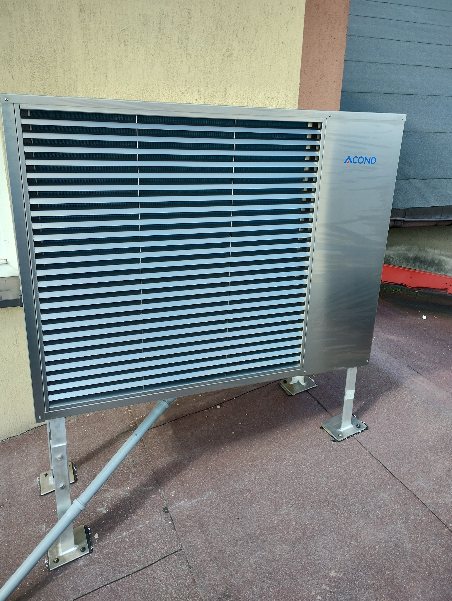 Zewnętrzna jednostka klimatyzacyjna marki ACOND, zamontowana na dachu, z widocznym odpływem kondensatu i elementami mocującymi do podłoża.