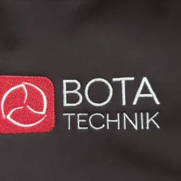 Czarny materiał z wyhaftowanym czerwonym logo i białym napisem 'BOTA TECHNIK', widoczne detale ściegów.