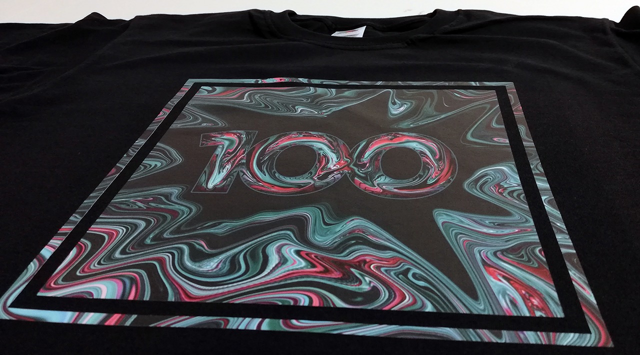 Czarna koszulka z nadrukiem cyfr '100' w kwadracie, wypełnionych abstrakcyjnym wzorem w odcieniach turkusu i czerwieni.