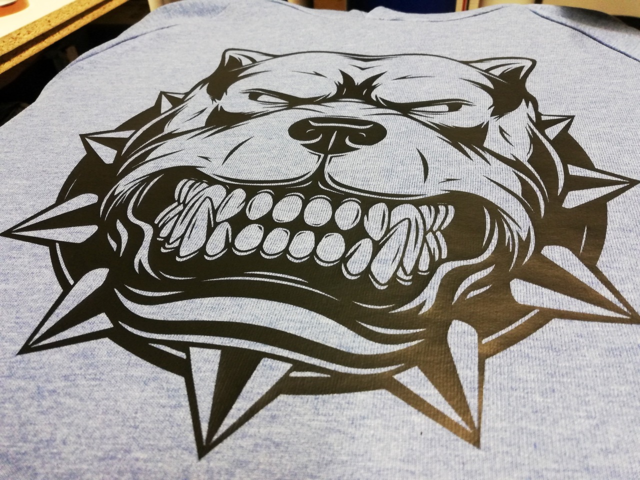 Jasnoniebieska koszulka z czarnym nadrukiem przedstawiającym groźnego psa z kolcami wokół głowy.