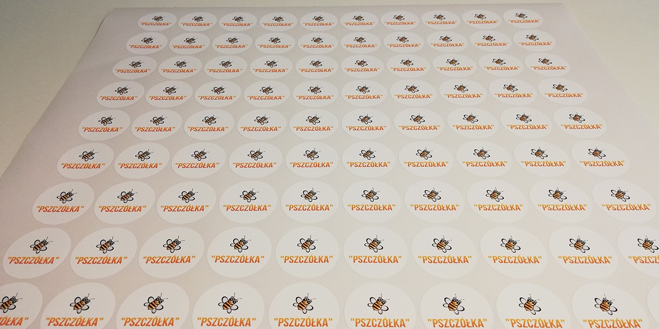 Arkusz z okrągłymi, samoprzylepnymi etykietami z logo pszczoły i napisem 'Pszczółka' wydrukowanymi w pomarańczowym kolorze.