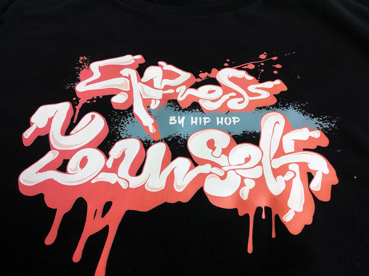 Czarna koszulka z nadrukiem 'Express Yourself By Hip Hop' w stylu graffiti z efektem rozprysku farby w kolorach białym, koralowym i turkusowym.