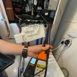 Mężczyzna z miernikiem GD-8 sprawdza szczelność kotła gazowego, widoczne otwarte wnętrze urządzenia z elementami instalacji.