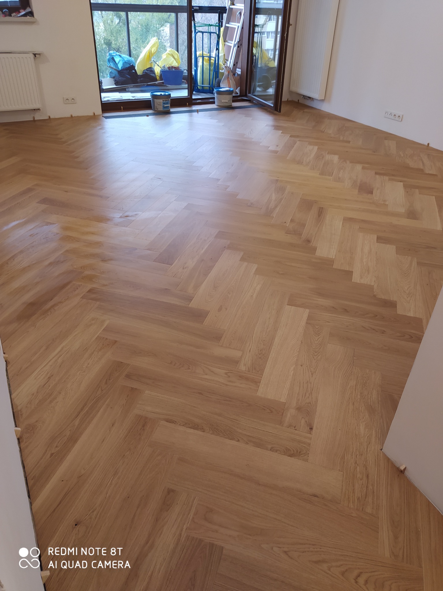 Ułożony parkiet w jodełkę francuską, widoczne wiaderka i drabina w tle, pokój po remoncie.