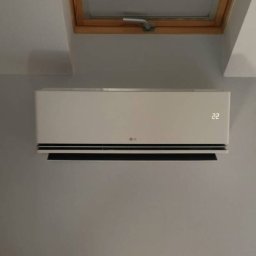 Śląski instytut chłodnictwa sp. z o.o. - Biała klimatyzacja LG zamontowana pod oknem dachowym na szarej ścianie. Widoczny wyświetlacz z temperaturą 22 stopnie. Minimalistyczny design.