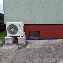 Śląski instytut chłodnictwa sp. z o.o. - Biała jednostka zewnętrzna klimatyzacji Rotenso zamontowana na betonowych podstawach przy ścianie budynku z niebieskim przewodem odprowadzającym skropliny.