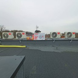Śląski instytut chłodnictwa sp. z o.o. - Rząd klimatyzatorów VIVAX na dachu budynku, z kartonem produktu i narzędziami obok. Widok z dołu, pochmurne niebo w tle. Instalacja klimatyzacji.