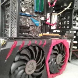 Wnętrze obudowy komputera stacjonarnego z widoczną kartą graficzną MSI z dwoma wentylatorami i czerwonymi akcentami, płytą gł&oacute;wną z elementami chłodzenia oraz dyskiem twardym.