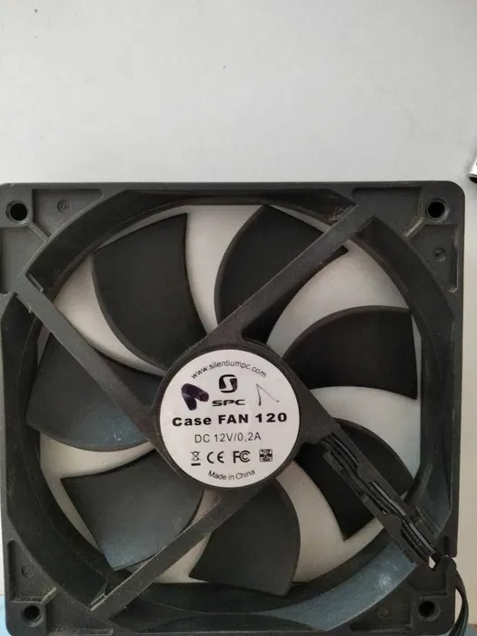 Czarny wentylator SPC Case FAN 120 z widocznymi śladami kurzu, leżący na jasnym tle. Widoczne logo i oznaczenia techniczne na naklejce centralnej.