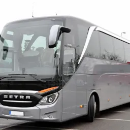 Nowoczesny, szary autokar marki Setra zaparkowany na parkingu, widok z przodu i boku, z widocznymi detalami jak reflektory i logo.