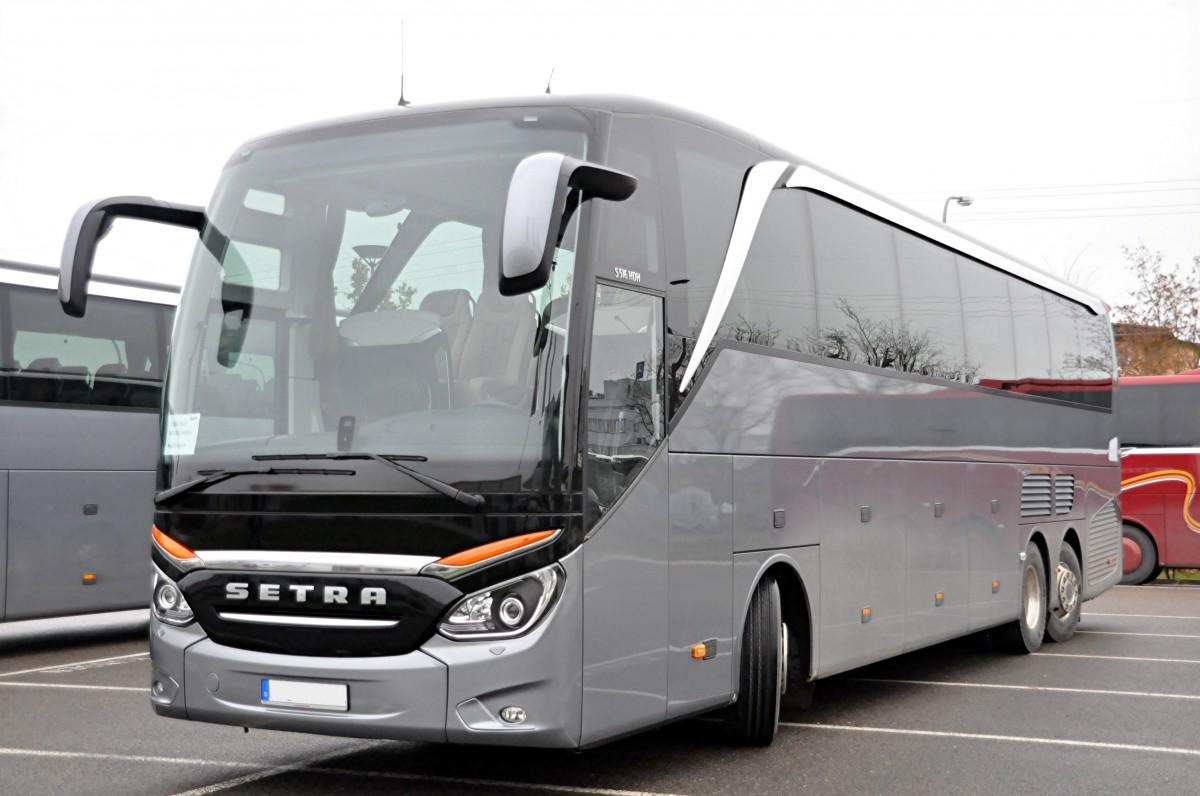 Nowoczesny, szary autokar marki Setra zaparkowany na parkingu, widok z przodu i boku, z widocznymi detalami jak reflektory i logo.