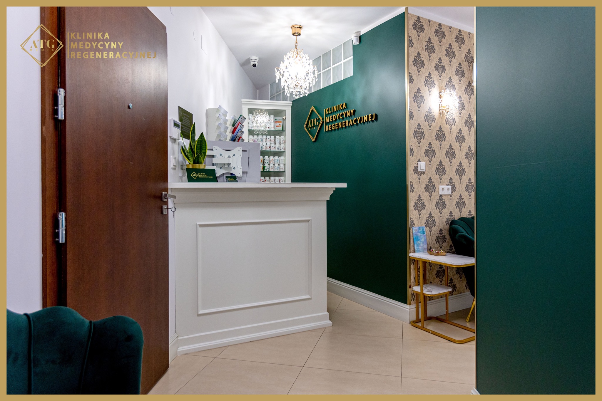 Wnętrze kliniki medycyny regeneracyjnej: biała recepcja z rośliną doniczkową, ściana w kolorze butelkowej zieleni z logo, kryształowy żyrandol, wzorzysta tapeta, ciemne drzwi wejściowe i fragment...