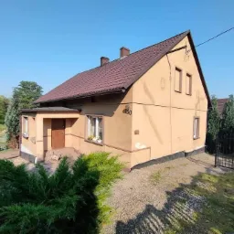 Dwukondygnacyjny dom jednorodzinny z brązowym dachem i elewacją w odcieniach beżu, numer domu 450, widoczny z poziomu gruntu, otoczony zielenią.