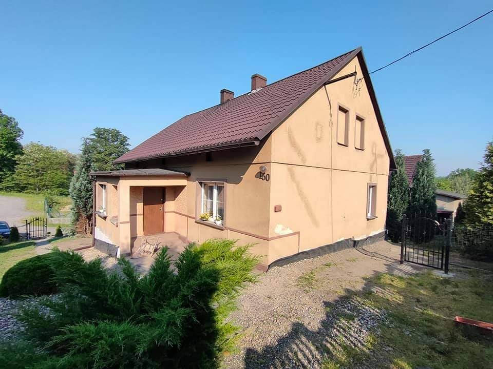 Dwukondygnacyjny dom jednorodzinny z brązowym dachem i elewacją w odcieniach beżu, numer domu 450, widoczny z poziomu gruntu, otoczony zielenią.