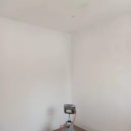 Wnętrze z białymi, świeżo pomalowanymi ścianami i drewnianą podłogą, w rogu stoi przenośny grzejnik gazowy.