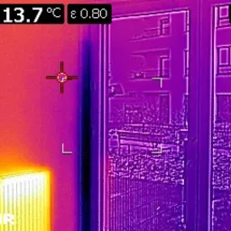 Termowizyjne zdjęcie ściany, okna i grzejnika w mieszkaniu, prezentujące rozkład temperatur i straty ciepła, wykonane kamerą FLIR.