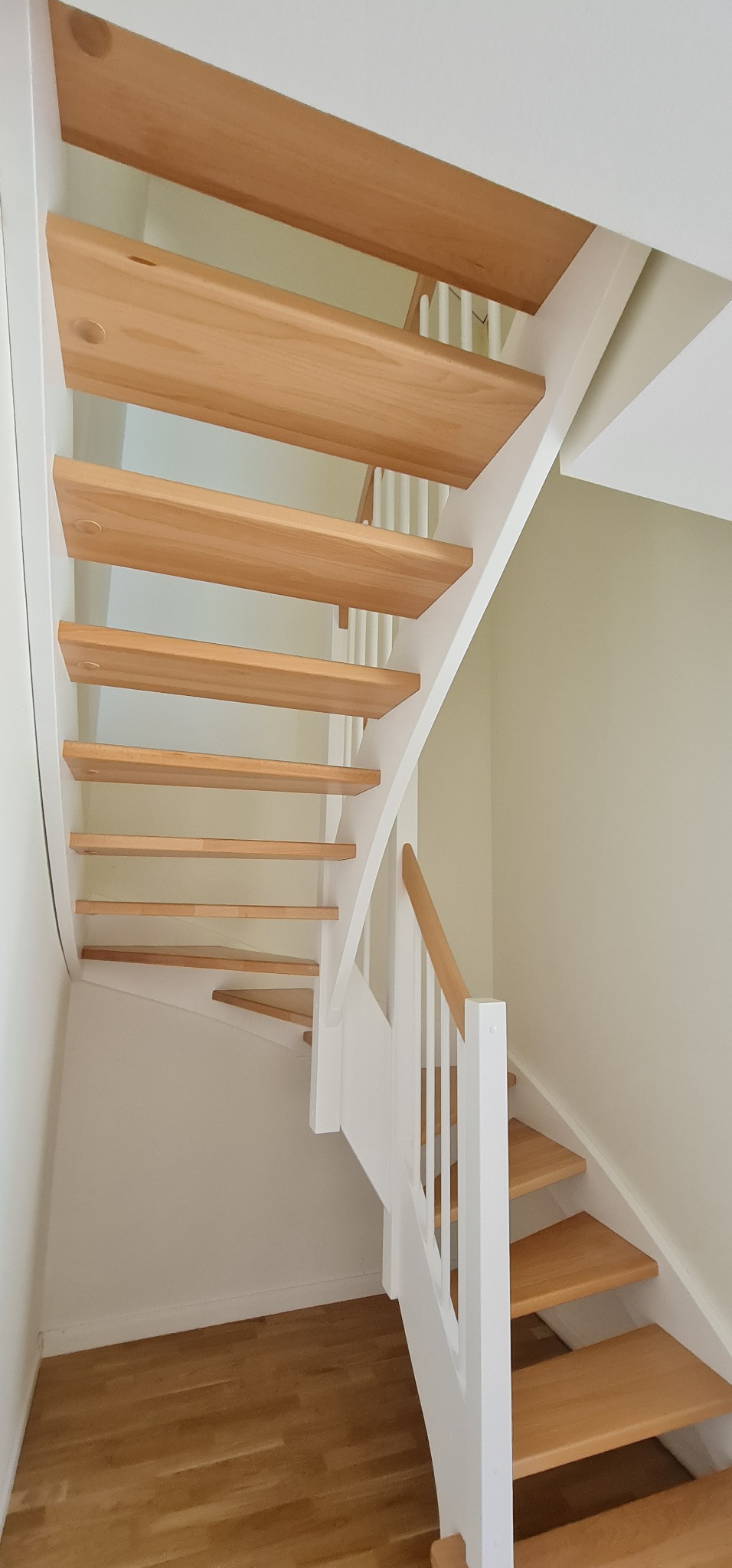 Drewniane schody z jasnego drewna z białymi elementami konstrukcyjnymi i balustradą, widok od dołu, widoczne stopnie i fragment podłogi.