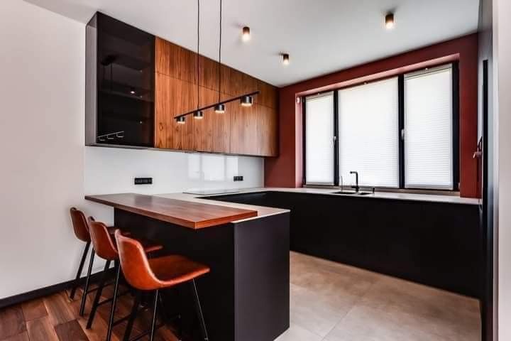 Nowoczesna kuchnia z drewnianymi szafkami górnymi, czarnymi szafkami dolnymi i blatem z drewna w części barowej, oświetlona listwą z pięcioma reflektorami