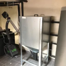 Szczegółowe ujęcie kotłowni z podajnikiem pelletu, widoczne rury instalacji grzewczej i zasobnik ciepłej wody użytkowej.