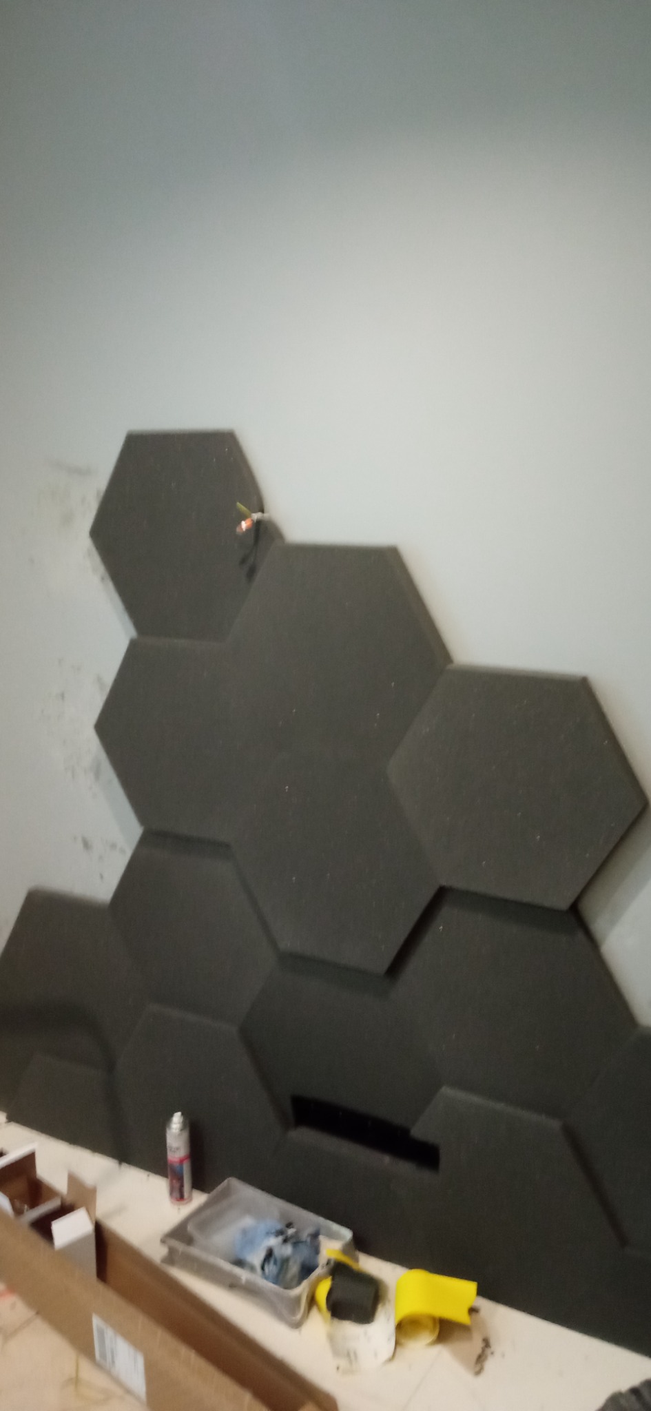 Montaż paneli akustycznych w kształcie heksagonów na ścianie, widoczne narzędzia i materiały przygotowane do dalszej pracy.