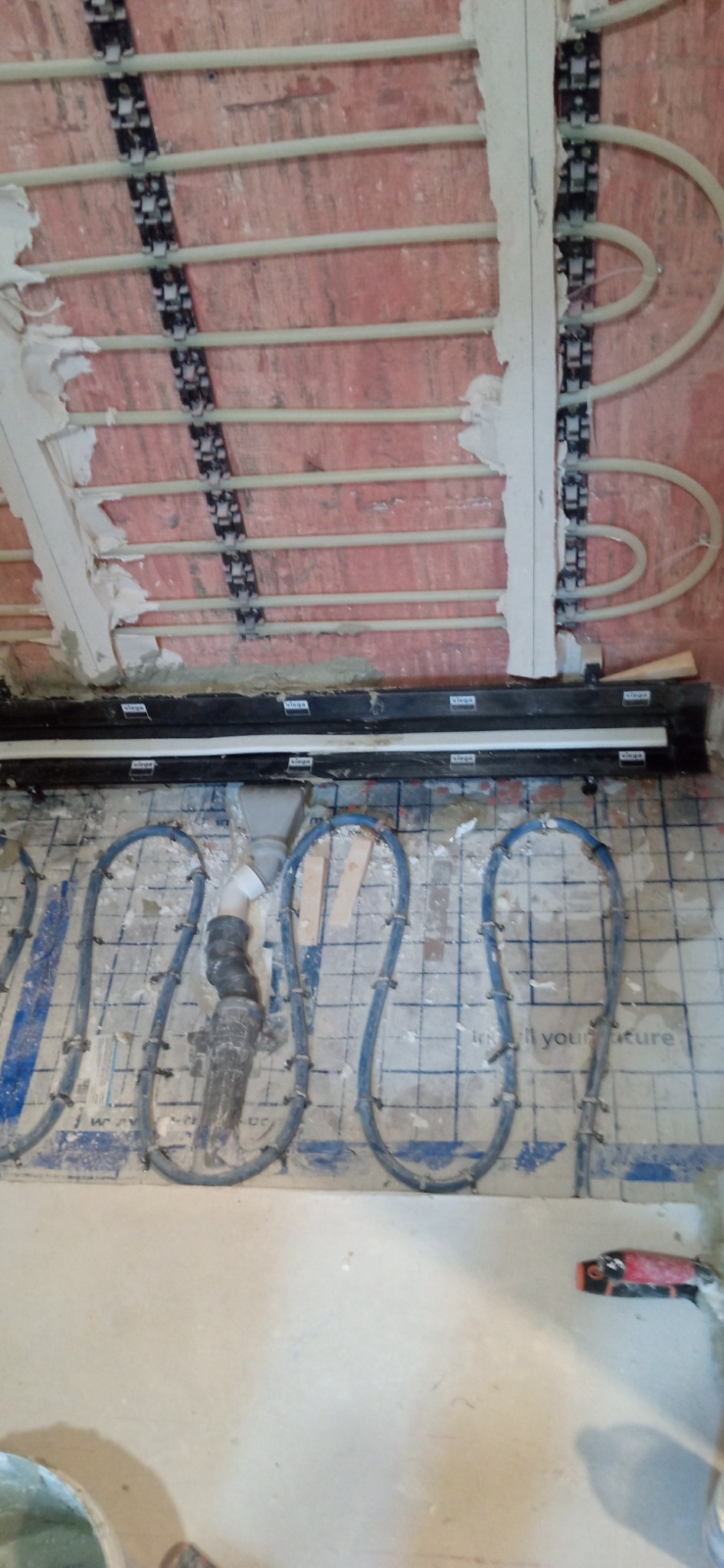 Montaż ogrzewania podłogowego i sufitowego z rurami w kształcie pętli mocowanymi do listew na ścianie i siatki na podłodze.