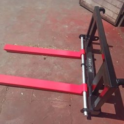 Patryk Żurek usługi spawalnicze MT-spaw - Widok z przodu na nowy, czarny wózek widłowy z czerwonymi widłami, stojący na czerwonej podłodze w pobliżu drewnianej ściany.