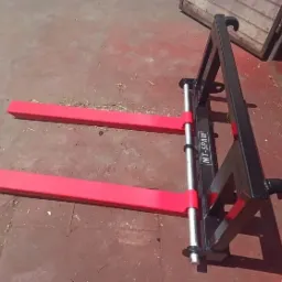 Widok z przodu na nowy, czarny wózek widłowy z czerwonymi widłami, stojący na czerwonej podłodze w pobliżu drewnianej ściany.