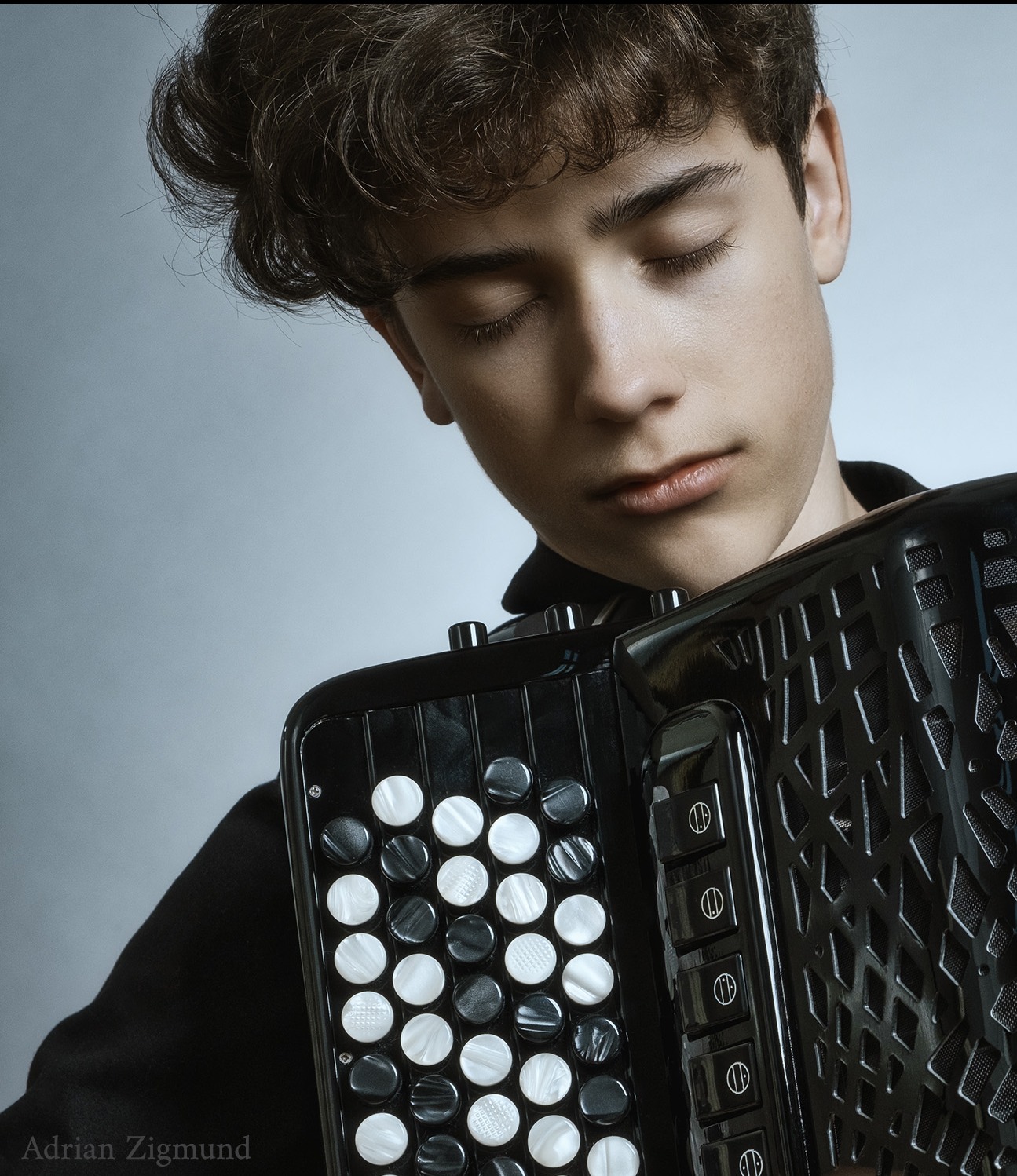 Portret młodego muzyka z zamkniętymi oczami, trzymającego akordeon. Stonowana kolorystyka i delikatne oświetlenie nadają zdjęciu artystyczny charakter.