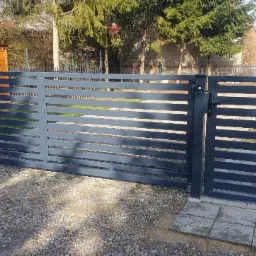 Nowoczesna, przesuwna brama wjazdowa z poziomych profili, pomalowana na grafitowo, z widoczną skrzynką na listy i fragmentem posesji w tle.