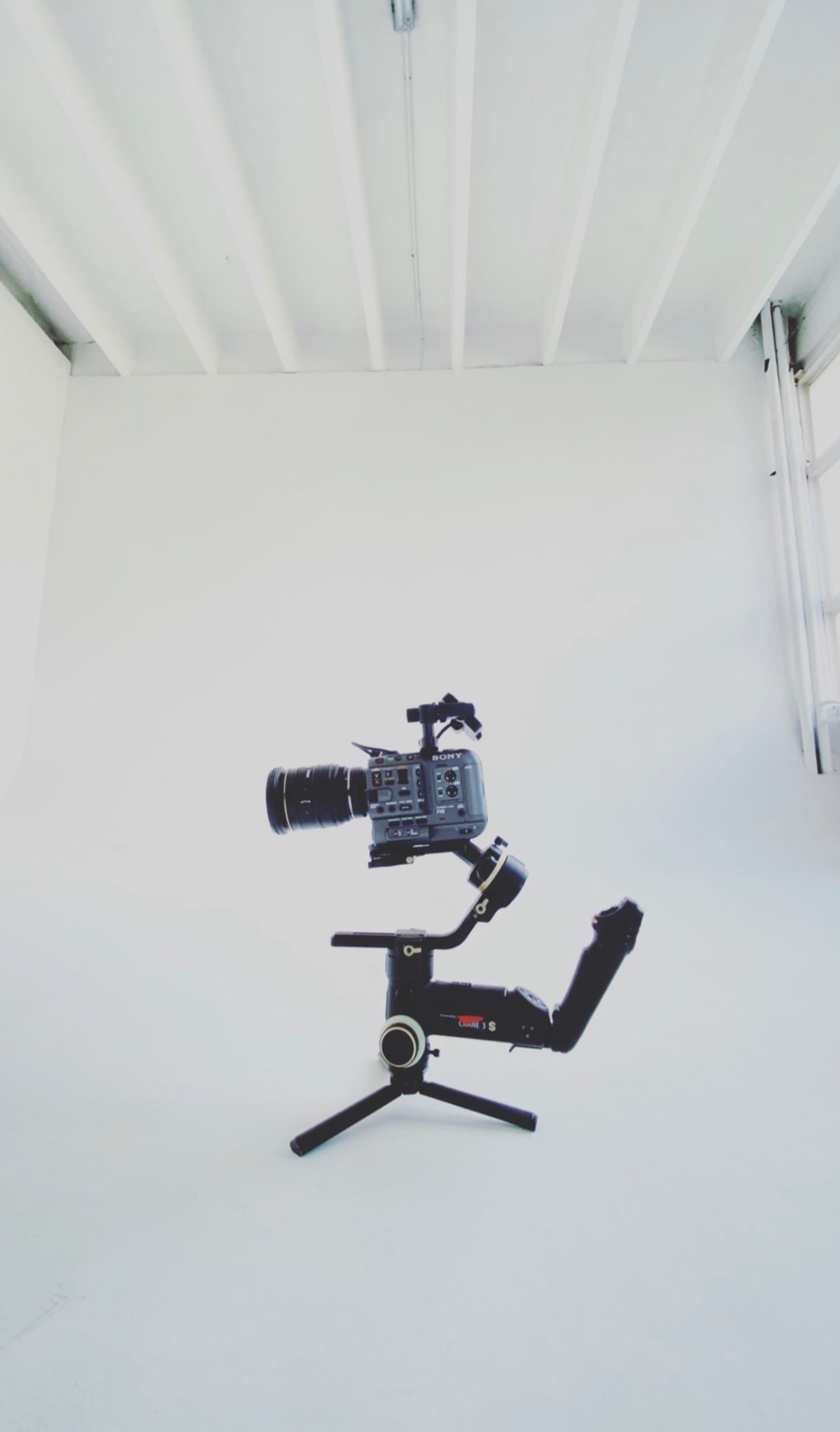 Profesjonalna kamera Sony z obiektywem i stabilizatorem Crane 3S ustawiona w białym studio filmowym z oknem.