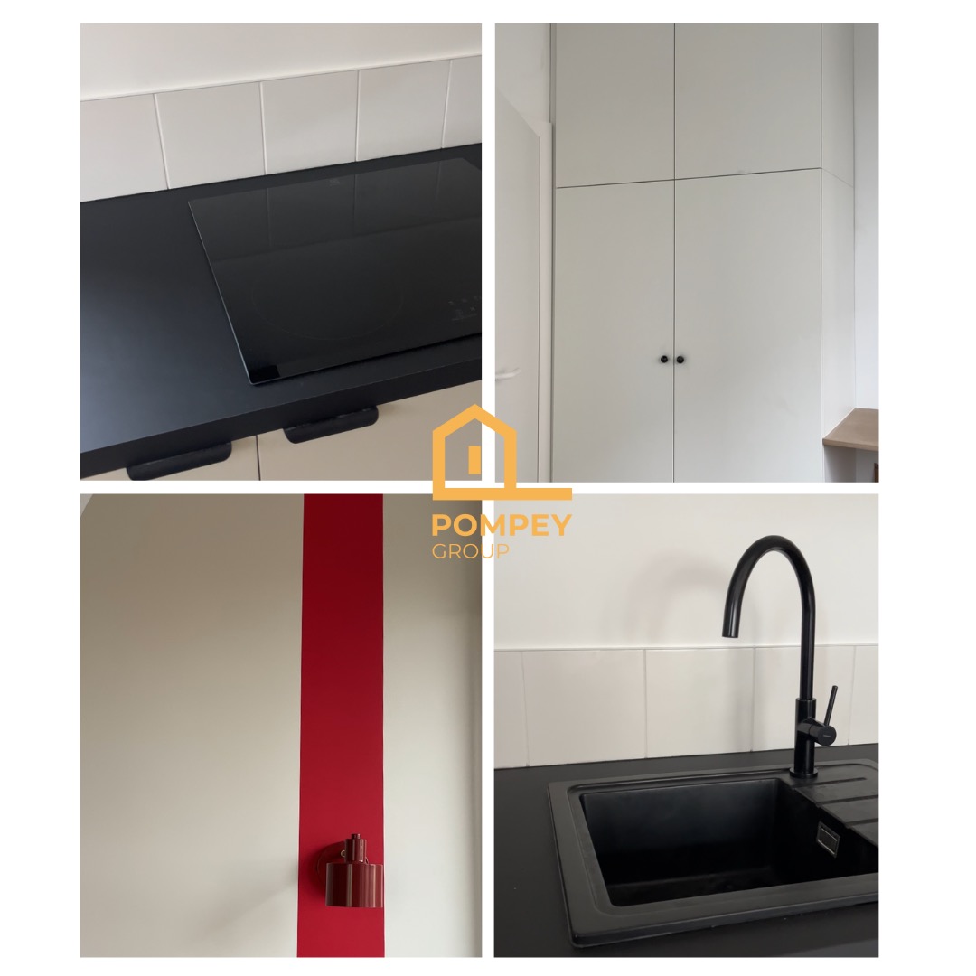Nowoczesna kuchnia po remoncie: czarny blat z płytą indukcyjną, białe szafki, czarny zlew z baterią i ściana z czerwonym akcentem. Minimalistyczny design.