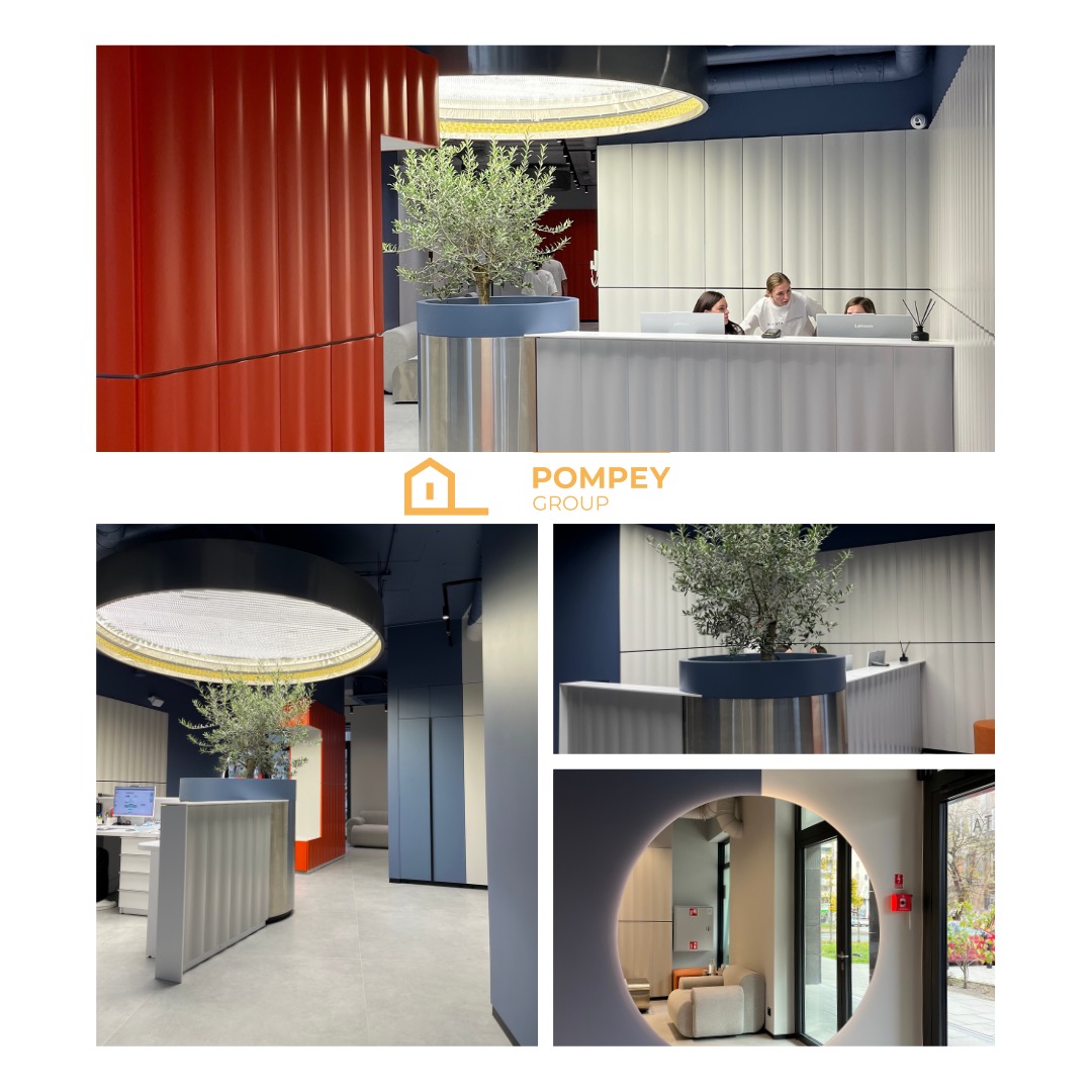 Nowoczesne wnętrze biurowe z recepcją, rośliną w donicy i oświetleniem LED. Kolorystyka: biel, granat i pomarańcz. Widoczne osoby za ladą.