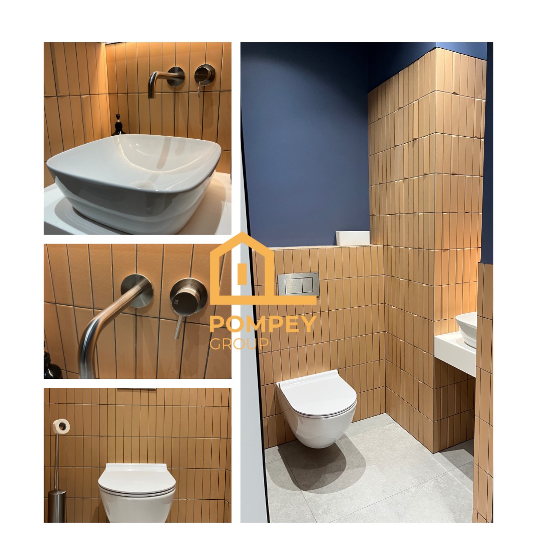 Nowoczesna łazienka z beżowymi, pionowo ułożonymi płytkami, wiszącą toaletą i umywalką nablatową. Ciemnoniebieska ściana dodaje kontrastu.