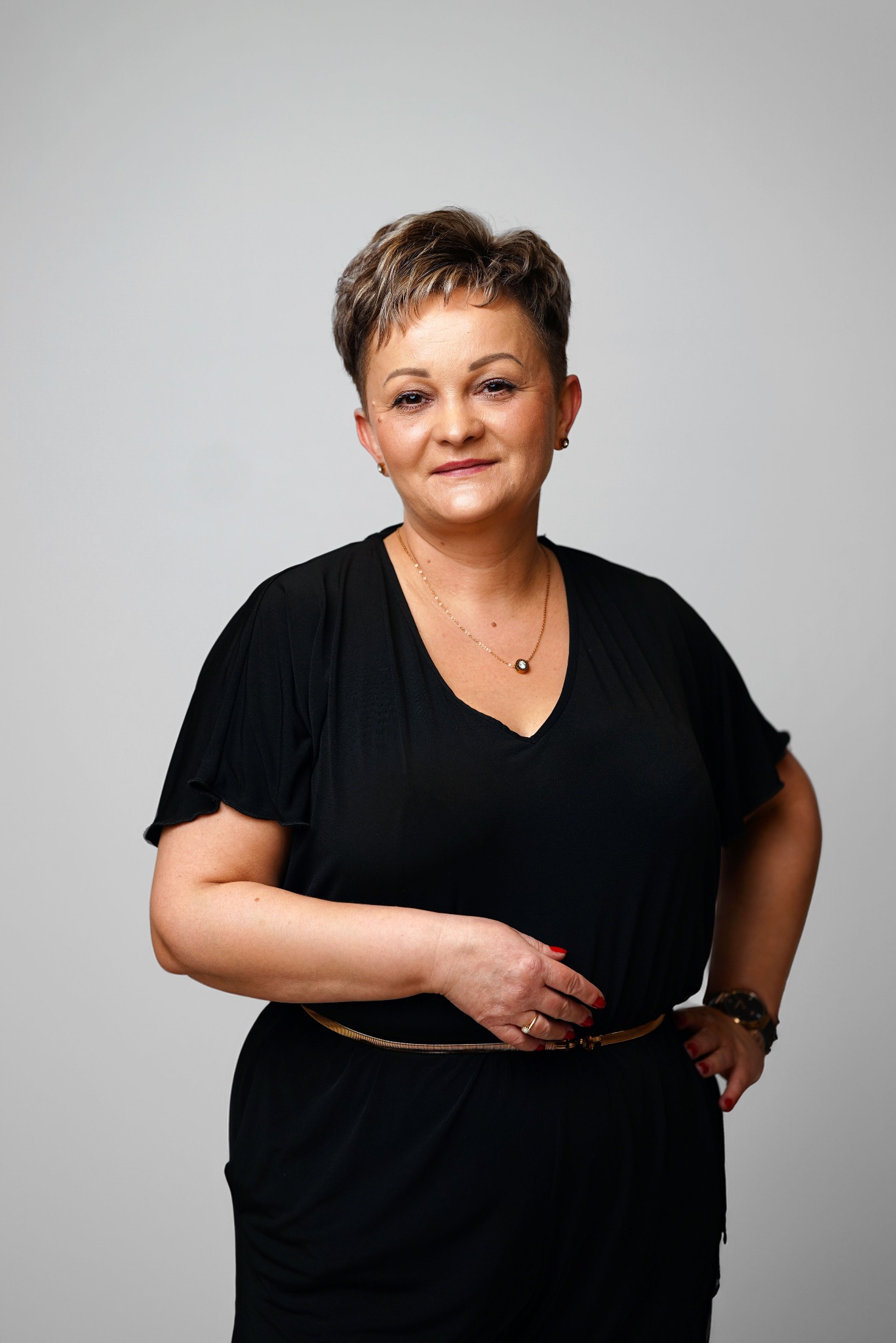 Portret kobiety w czarnej sukience z paskiem, na jasnym tle. Uśmiechnięta, z krótkimi włosami. Zdjęcie wykonane w Białymstoku.