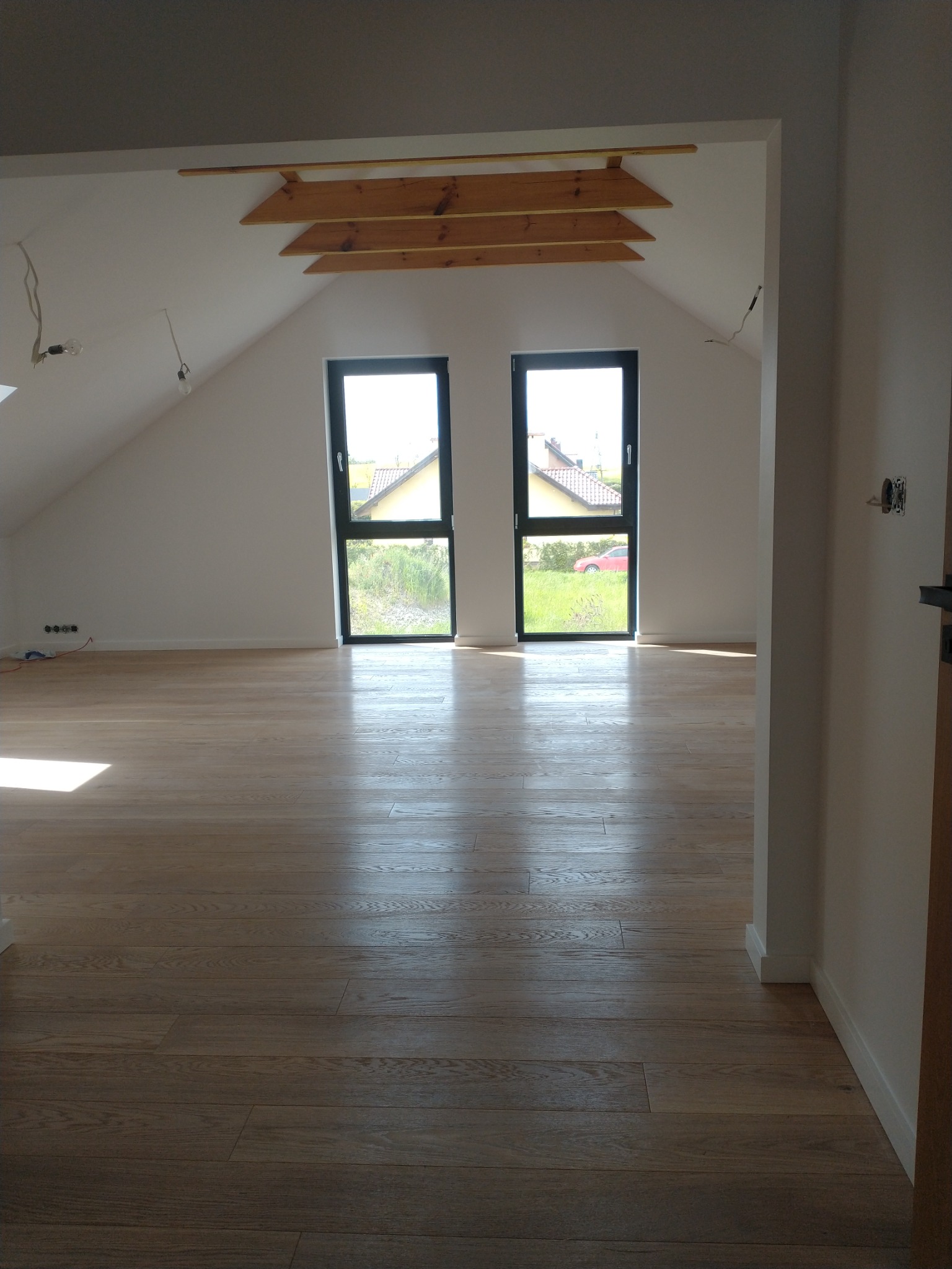Poddasze w Pniewach z drewnianą podłogą i dwoma oknami, widoczne elementy konstrukcyjne dachu i przygotowane instalacje elektryczne.
