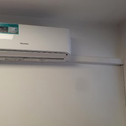 Dariusz Andreasik - Biały klimatyzator Hisense zamontowany na jasnej ścianie w pomieszczeniu biurowym, widoczne okno z zimowym krajobrazem na zewnątrz.