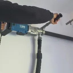 Pracownik w Jaśle wierci otwór w ścianie za pomocą wiertnicy diamentowej z odsysaniem pyłu, przygotowując miejsce pod instalację.