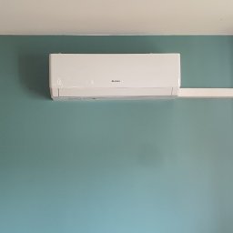 Dariusz Andreasik - Biała klimatyzacja Gree zamontowana na turkusowej ścianie w pokoju z półkami i obrazami winyli.