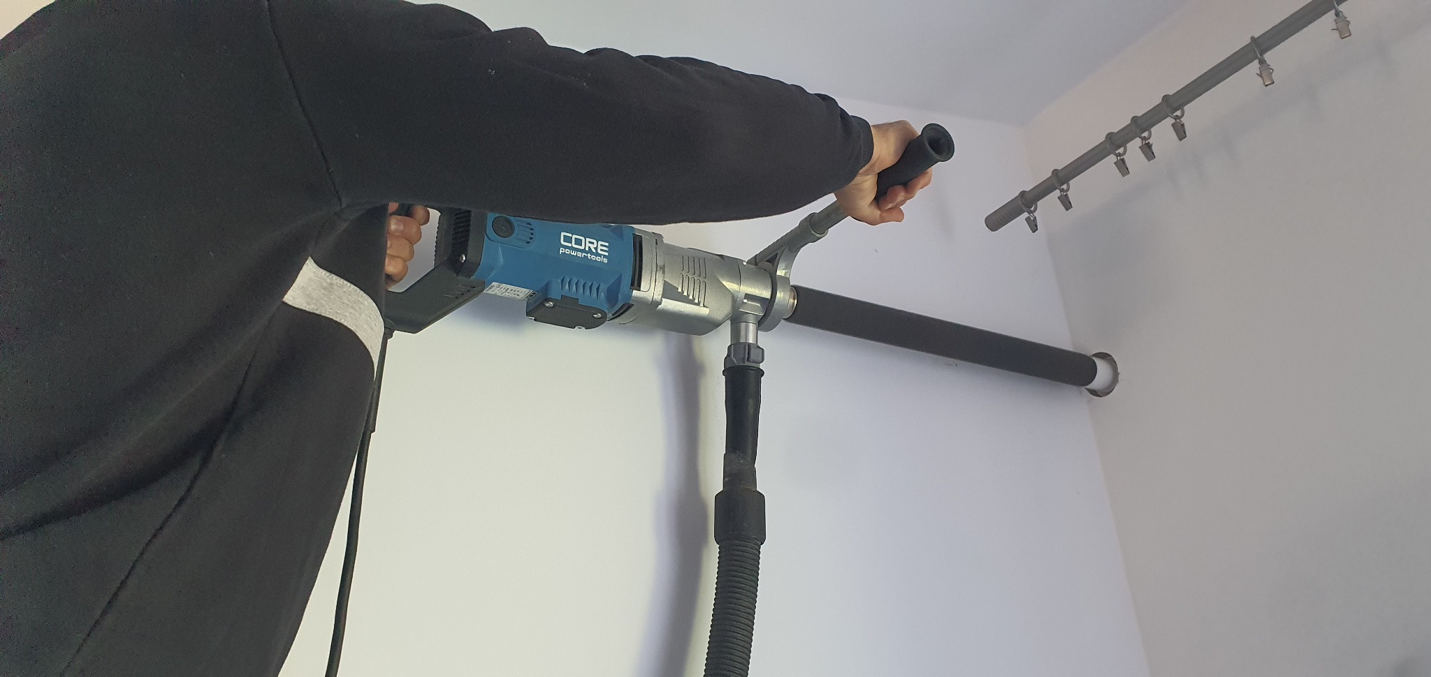 Pracownik w Jaśle wierci otwór w ścianie za pomocą wiertnicy diamentowej z odsysaniem pyłu, przygotowując miejsce pod instalację.