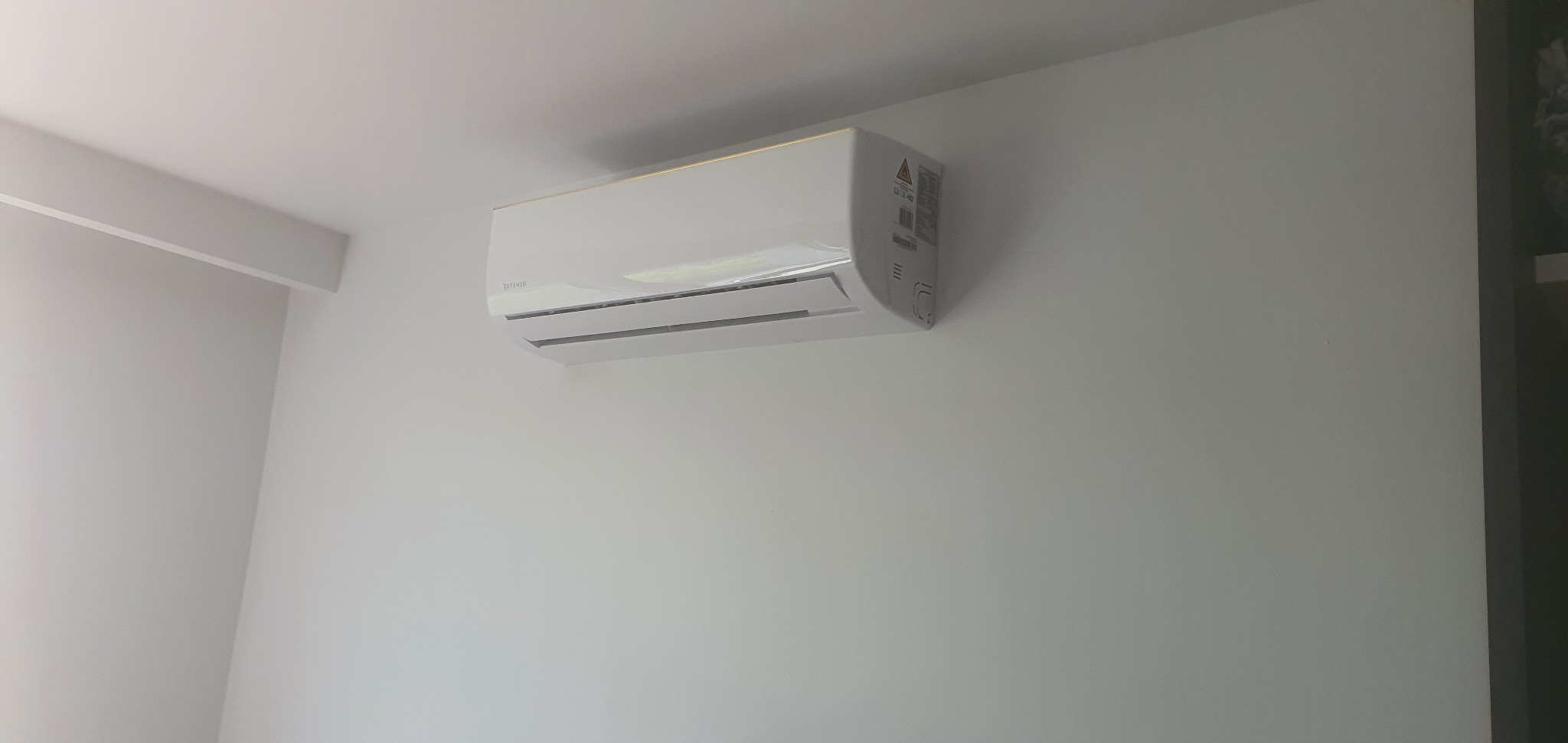 Biała jednostka wewnętrzna klimatyzacji marki Rotenso zamontowana na jasnej ścianie w pomieszczeniu.