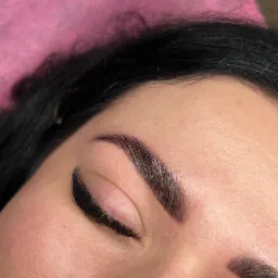 Zbliżenie na oko z ciemnymi, świeżo wystylizowanymi brwiami i przedłużonymi rzęsami na tle różowego podkładu.