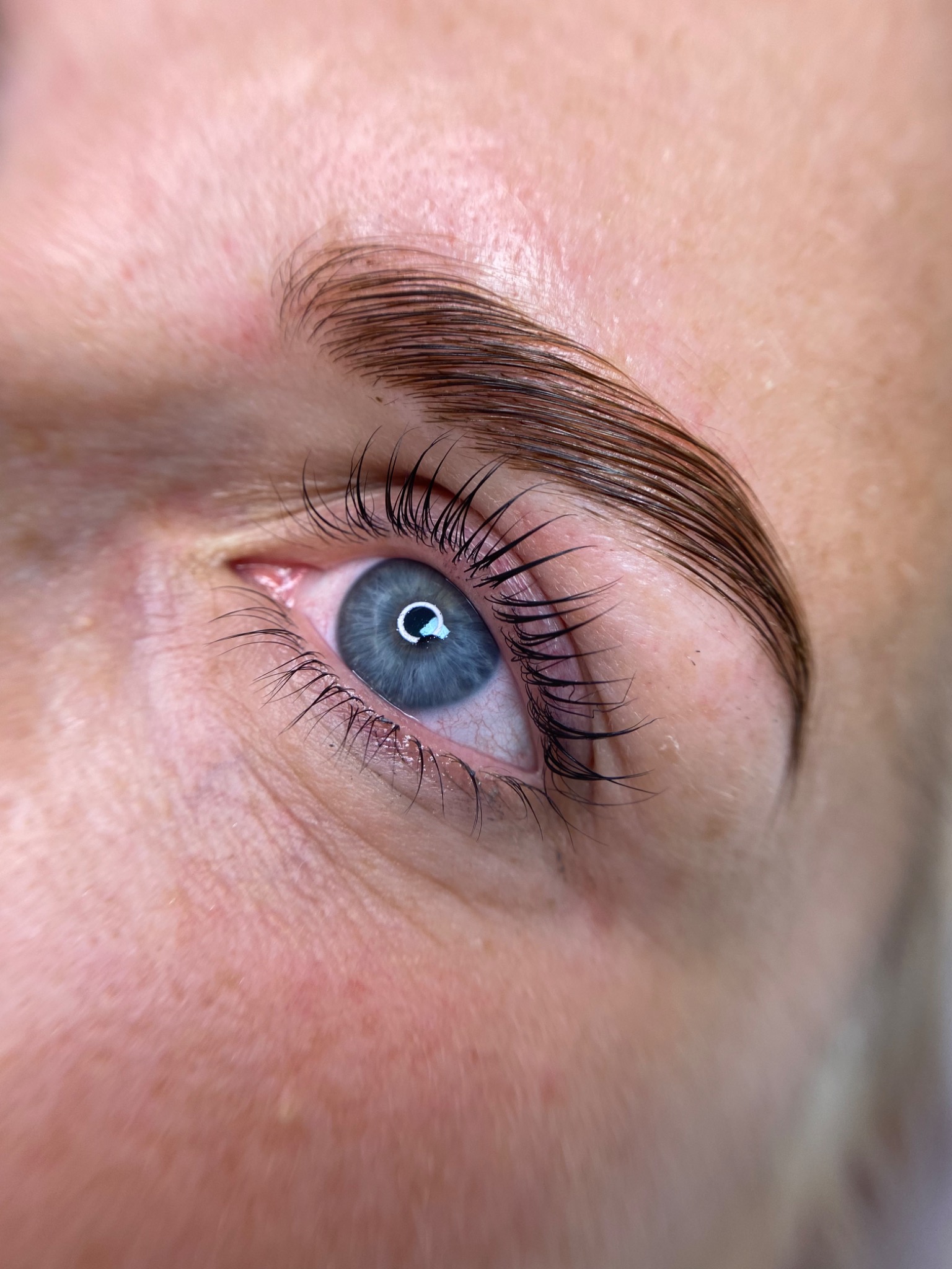 Zbliżenie na oko z wyraźnie podkręconymi rzęsami i wystylizowaną brwią, widoczne drobne włoski i szczegóły skóry.