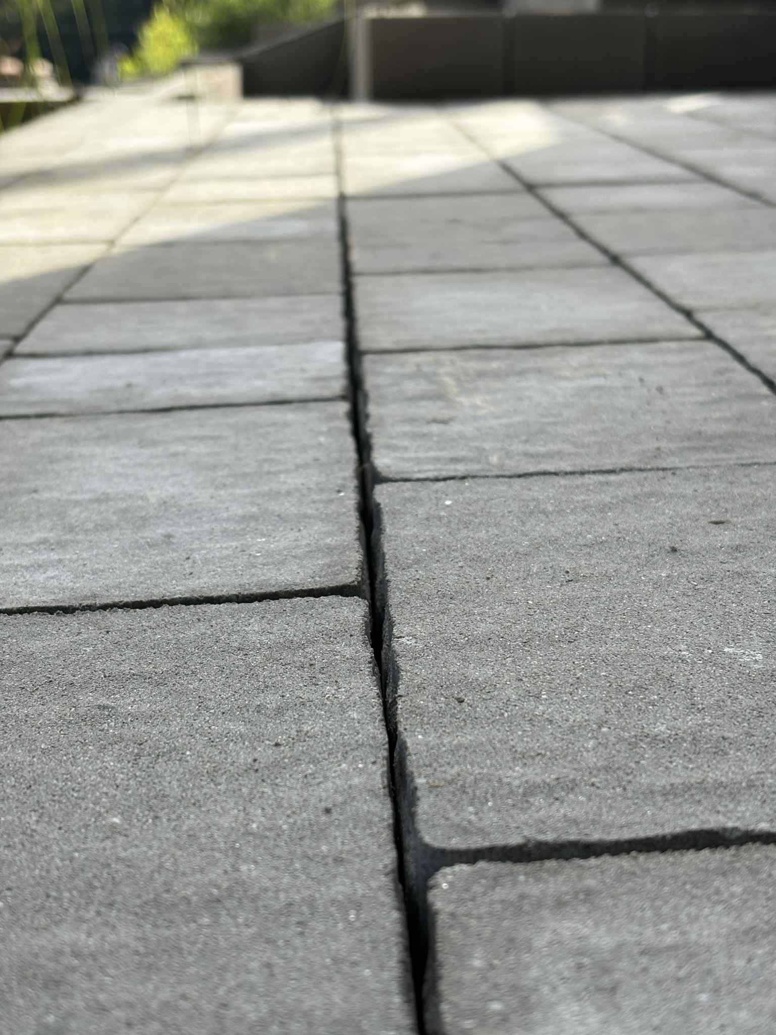 Szara kostka brukowa ułożona w regularny wzór, widok z bliska z niskiego kąta, podkreślający teksturę i precyzję wykonania. Minimalistyczne tło.