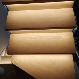 Michał Wyszyński - Drewniane schody z podświetleniem LED na każdym stopniu, widok z góry, ciepłe barwy.