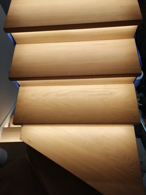 Drewniane schody z podświetleniem LED na każdym stopniu, widok z góry, ciepłe barwy.