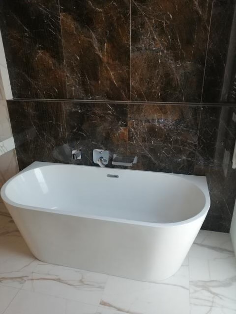 Nowoczesna, wolnostojąca wanna w łazience wykończonej marmurowymi płytkami w odcieniach brązu i bieli.