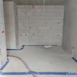 Surowy stan wnętrza w trakcie prac elektrycznych: widoczne przewody w peszlach ułożone wzdłuż ścian i wyprowadzenia kabli ze ścian, ściany z betonu komórkowego.