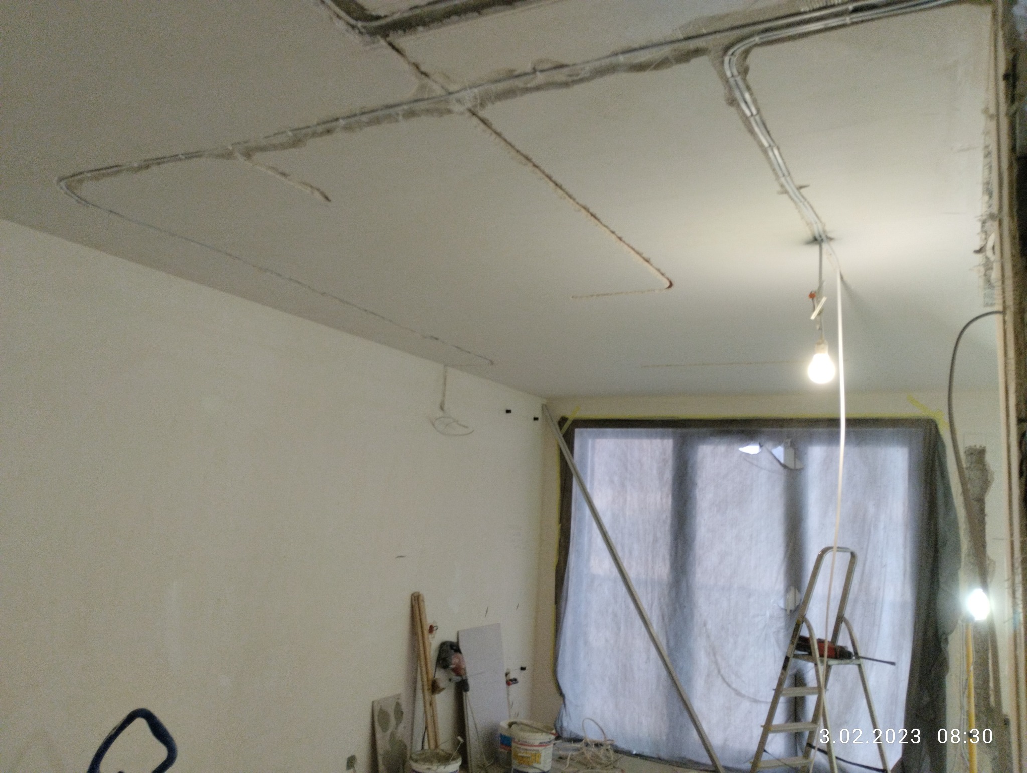 Wnętrze w trakcie prac wykończeniowych: widoczne przewody elektryczne w bruzdach na suficie, drabina oparta o okno zabezpieczone folią, oraz narzędzia i materiały budowlane.